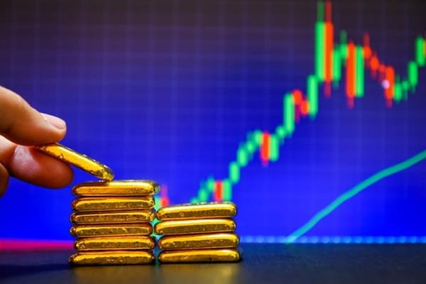 Hand placing gold bars on a stack with a rising financial market chart in the background.
